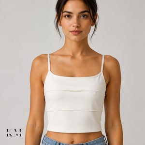May include: A solid white cropped camisole top featuring a square neckline, thin shoulder straps, and two horizontal layered fabric panels across the chest. The garment has a fitted silhouette and a clean, smooth finish throughout the bodice.
