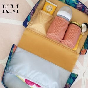 May include: A floral print baby bottle organizer with multiple compartments. The organizer has a mustard yellow interior and includes a bottle, jar, spoon, and a small packet. The exterior features a blue floral pattern.