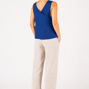 May include: A sleeveless royal blue top featuring a V-neckline and a wrap-style back design, paired with loose-fitting beige trousers. The top has a solid color and a textured fabric appearance, while the trousers are straight-legged and neutral.