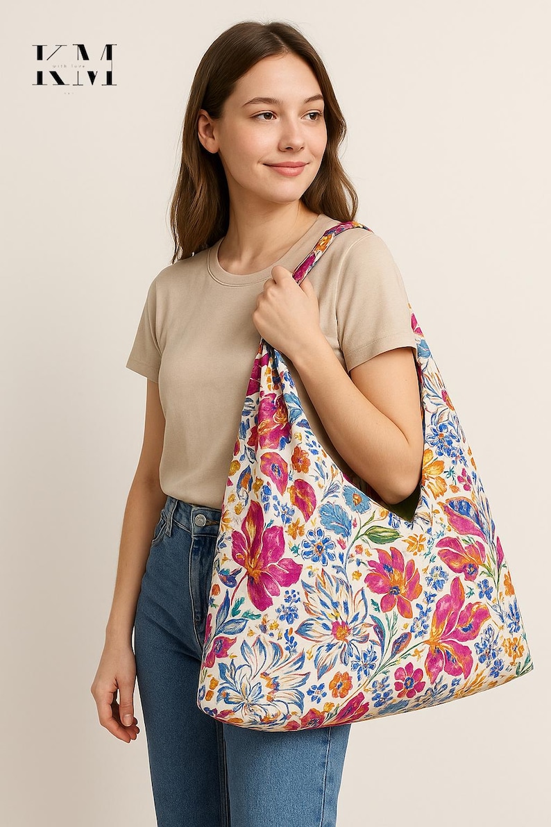 May include: A floral tote bag with a white background and large pink, blue, and orange flowers. The bag is held by a person wearing a beige t-shirt and blue jeans. The bag's strap has a floral pattern.