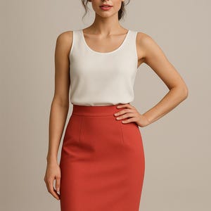 Puede incluir: Una mujer con una camiseta sin mangas blanca con cuello redondo y una falda lápiz color óxido. La falda llega a la rodilla y tiene un corte entallado. El atuendo es sencillo y elegante, adecuado para un entorno profesional.