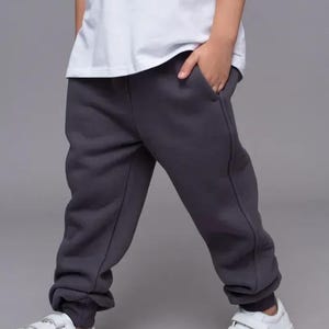 May include: A person wearing a white t-shirt and dark gray sweatpants. The person is also wearing white sneakers with velcro straps. The image has the letters "KM" in the upper left corner.