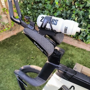 Puede incluir: Bicicleta de triatlón en blanco y negro con una botella de agua blanca. La bicicleta tiene manillar negro y un asiento negro. La botella de agua tiene el texto "226ERS" y "PROFILE DESIGN". La bicicleta está sobre un césped verde.