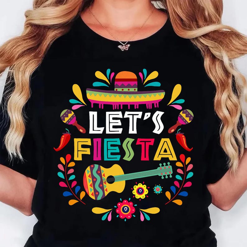 May include: Black t-shirt with a colorful "Let's Fiesta" design. The graphic includes a sombrero, maracas, chili peppers, a guitar, and floral elements. The design is vibrant with yellow, red, green, and blue.