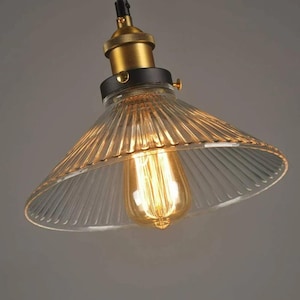 May include: A clear glass pendant light shade with a ribbed design. The shade is attached to a black metal fixture with a gold-colored base.