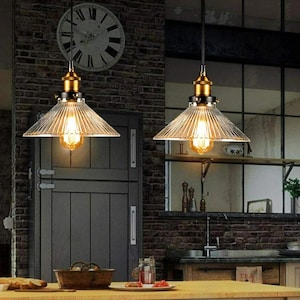 May include: Two vintage-style pendant lights with clear glass shades and brass accents hang over a kitchen counter. The shades have a ribbed texture and the lights are turned on, illuminating the space.