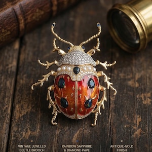 May include: Vintage jeweled beetle brooch with a rainbow sapphire and diamond pave design. The brooch has an antique-gold finish. The beetle's body is red and orange with black accents, and the head is covered in small, sparkling stones.