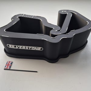 May include: Black, angular container with the word "SILVERSTONE" in white. The container has a unique shape with white accent lines. A small Union Jack flag on a black stick is next to the container.