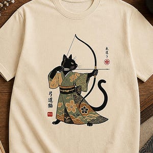 May include: A beige short-sleeved t-shirt featuring a graphic of a black cat wearing a patterned kimono and aiming a bow and arrow. The design includes Japanese text and a red seal. The cat is depicted in a focused stance with its tail curved.