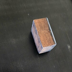 May include: A wooden block with a light brown color and a dark brown wood grain. The block has a thin silver metal trim around the edges.