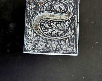 May include: A close-up of a silver metal stamp with an ornate letter "S" design. The stamp is on a black background with the text "BLACK BEAUTY TRADE MARK REG. U.S. 57106".
