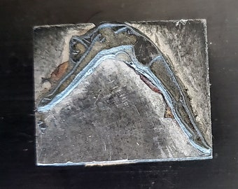 May include: A black and white image of a person diving into water. The image is printed on a metal surface.