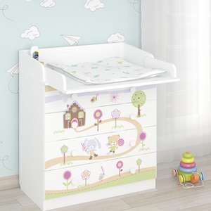 Può includere: Cassettiera bianca per neonati con un design stravagante. I cassetti presentano illustrazioni di una casa, animali e una strada tortuosa. Un giocattolo multicolore è sul pavimento. La cassettiera ha un fasciatoio sopra.