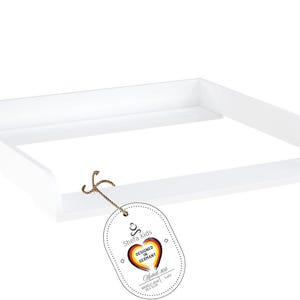Könnte beinhalten: Weißer Wickeltisch-Aufsatz mit einem kleinen Etikett mit der Aufschrift "Shefla Kids Designed in Germany"