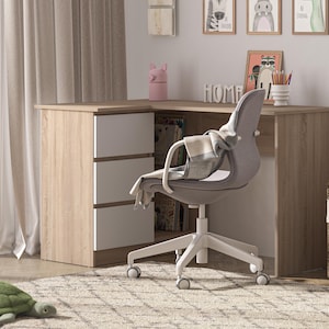 Könnte beinhalten: Ein Eckschreibtisch in hellem Holzton mit weißen Schubladen, ein grauer Bürostuhl und ein geflochtener Korb mit einem Stoffbären. Der Schreibtisch hat einen kleinen rosa Behälter und einen Stifthalter. Ein grünes schildkrötenförmiges Kissen liegt auf dem Boden.