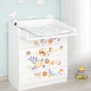 Könnte beinhalten: Weiße Wickelkommode mit Wickelauflage, verziert mit Blumen- und Vogelaufklebern in Orange, Gelb und Lila. Ein mehrfarbiges Spielzeug steht auf dem Boden neben dem Tisch. Ein Regal mit Dekoration ist an der Wand befestigt.