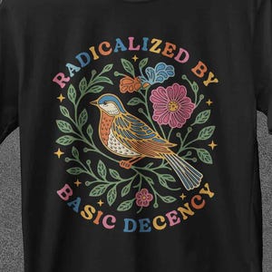 Könnte beinhalten: Schwarzes T-Shirt mit einem farbenfrohen Design eines Vogels, Blumen und dem Text "RADICALIZED BY BASIC DECENCY" in einem Kreis. Der Markenname "JoJoTeez" ist oben zu sehen.