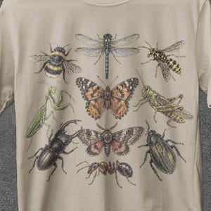 Op de afbeelding: Beige t-shirt met een gedetailleerde insectenillustratie, waaronder een vlinder, een libelle en een bij. Het shirt heeft de tekst "JoJoTeez", "BULK SALE" en "BUY 3 GET FREE SHIPPING".
