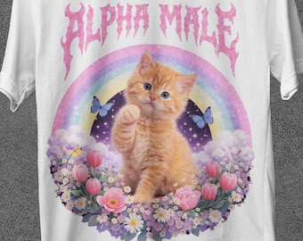 May include: White t-shirt featuring a cartoon kitten with a rainbow, butterflies, and flowers. The text "ALPHA MALE" is above the kitten in a pink, gothic font. The shirt has a round neck and short sleeves.