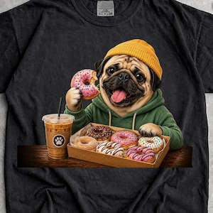 May include: A black t-shirt featuring a graphic of a pug wearing a yellow beanie and a green hoodie. The pug is holding a pink frosted donut, with a box of assorted donuts and a plastic cup of iced coffee placed on a wooden surface in front of it.