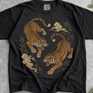 Peut inclure: T-shirt noir avec une illustration détaillée de deux tigres dans un motif circulaire avec des nuages et du bambou. Le texte "JoJoTeez" est en haut. Le mot "Black" est en bas.