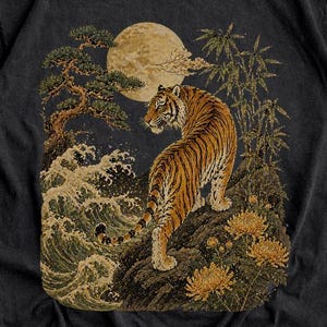 Pode incluir: Camiseta preta com uma ilustração de um tigre em frente a uma lua cheia e ondas. O design inclui bambu e flores. O texto "JoJoTeez" está no topo e "Black" na parte inferior da camiseta.