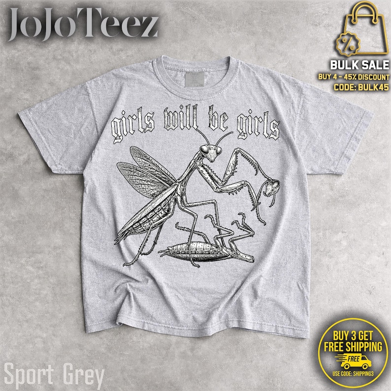 May include: A light gray short-sleeve t-shirt featuring a black ink-style illustration of a praying mantis standing over another insect. The text "girls will be girls" is printed in a gothic-style font above the graphic on the front of the shirt.