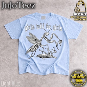 May include: A light blue t-shirt featuring a black and white graphic illustration of a praying mantis standing over another insect. The text "girls will be girls" is printed in a stylized black font above the insect illustration.
