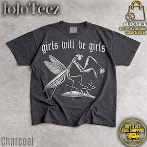May include: A charcoal gray short-sleeve t-shirt featuring a white line-art illustration of a praying mantis standing over another insect. The text "girls will be girls" is printed in a white gothic-style font above the insect graphic.