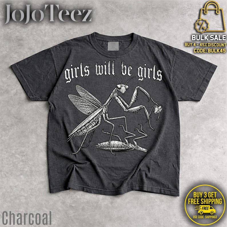May include: A charcoal gray short-sleeve t-shirt featuring a white line-art illustration of a praying mantis standing over another insect. The text "girls will be girls" is printed in a white gothic-style font above the insect graphic.