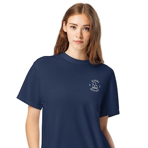 Può includere: T-shirt blu navy con una piccola grafica bianca sul petto sinistro. La grafica include il testo "KAORI" sopra un cuore stilizzato e la parola "KOUSEI" sotto. La maglietta ha maniche corte e girocollo.