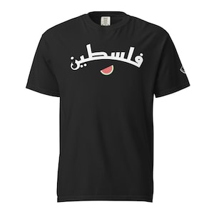 May include: Black t-shirt with white Arabic script and a watermelon slice graphic. The script reads "Palestine". The shirt is a crew neck and has a small logo on the sleeve.