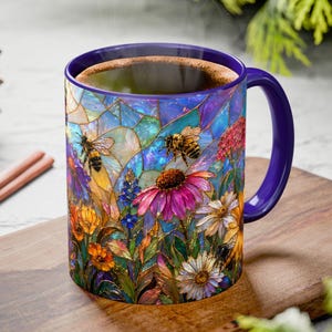 May include: A ceramic mug with a vibrant floral and bee design. The mug features a purple handle and rim, and is filled with a dark liquid. The colorful design includes flowers and bees, creating a nature-inspired theme.