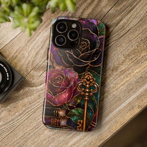 May include: A smartphone case featuring a dark, stained-glass style design with deep purple and black roses, green leaves, and a prominent metallic gold skeleton key. The artwork includes subtle book spines at the bottom with gold accents.