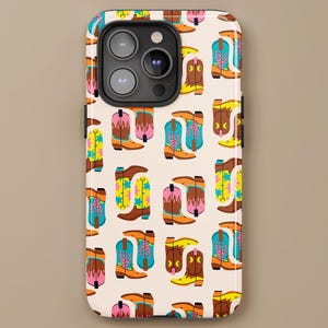 May include: A phone case with a repeating pattern of colorful cowboy boots in shades of brown, pink, yellow, and blue. The boots have various decorative elements, including stars and floral designs. The case has a light beige background and the brand name "LILOU" is at the bottom.