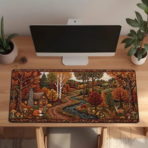 May include: A rectangular desk mat featuring a detailed autumn forest illustration with a log cabin, a winding stream, a fox, and a deer. The scene is filled with vibrant orange, red, and yellow trees, surrounded by a decorative border of fall leaves.