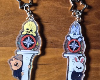 May include: Four clear acrylic keychains with star-shaped clasps. Each keychain features a cartoon animal design, including a bear, bunny, chick, and dog, with a compass rose design. The keychains are on a wooden surface.