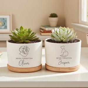 May include: Two white ceramic plant pots with succulents, each on a wooden base. One pot features a dog illustration and the name "Oliver", the other has a dog illustration and the name "Jasper". Both pots have the text "Never Forgotten".