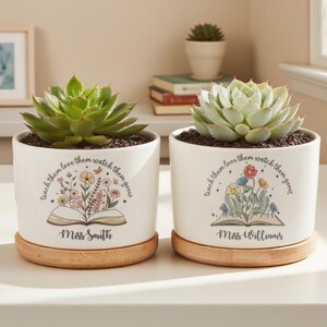 May include: Two white ceramic plant pots with succulents, each on a wooden base. The pots have the text "teach them love them watch them grow" and a floral design with the names "Miss Smith" and "Miss Williams".