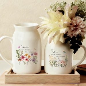 May include: Two white ceramic vases with handles, one larger than the other, sit on a wooden tray. The larger vase has the text "If Grandmas were flowers, I'd pick you." and a floral design. The smaller vase has the text "If Moms were flowers, I'd pick you." and a floral design.