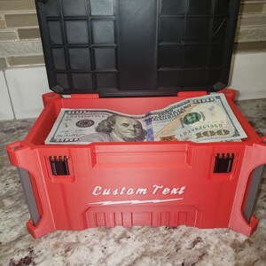 May include: Red storage box with a black lid, open to reveal several one hundred dollar bills. The box has the words "Custom Text" printed on the front.