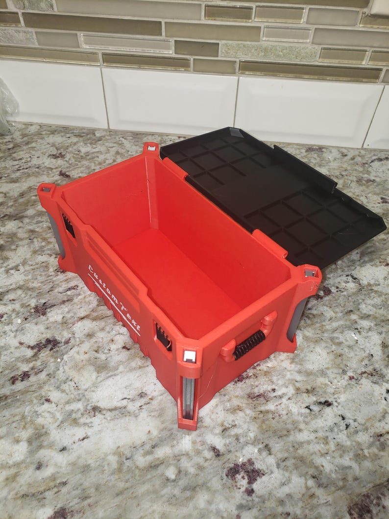 May include: Red plastic storage container with a black lid. The container has the words "Custom Text" printed on the side. The container is open, revealing the interior. The container is sitting on a marble surface.