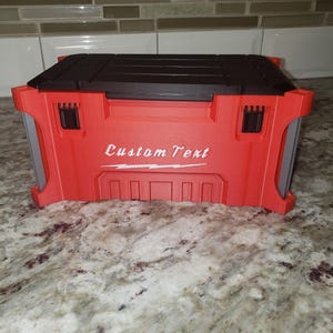 May include: A red and black toolbox with the words "Custom Text" in white script. The toolbox has a black top and red body with gray side panels. The toolbox is on a granite countertop.