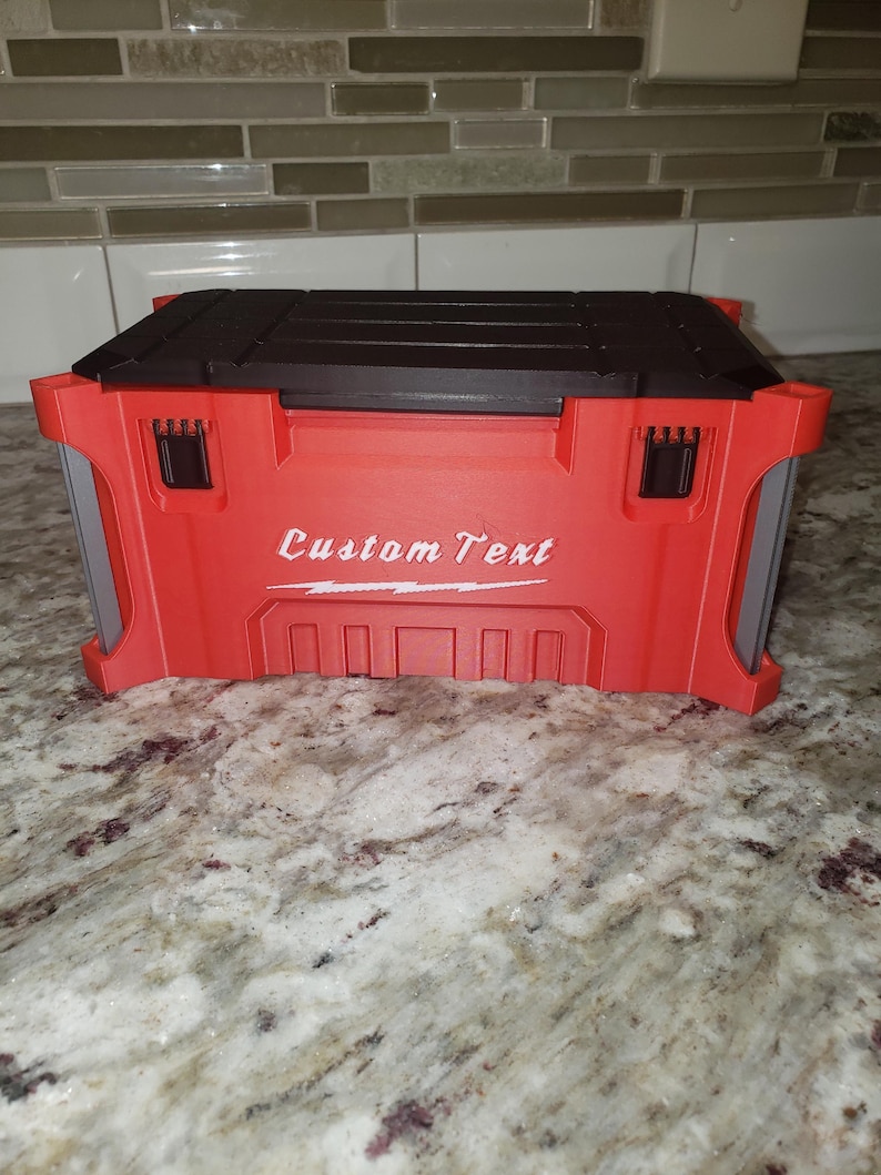 May include: A red and black toolbox with the words "Custom Text" in white script. The toolbox has a black top and red body with gray side panels. The toolbox is on a granite countertop.