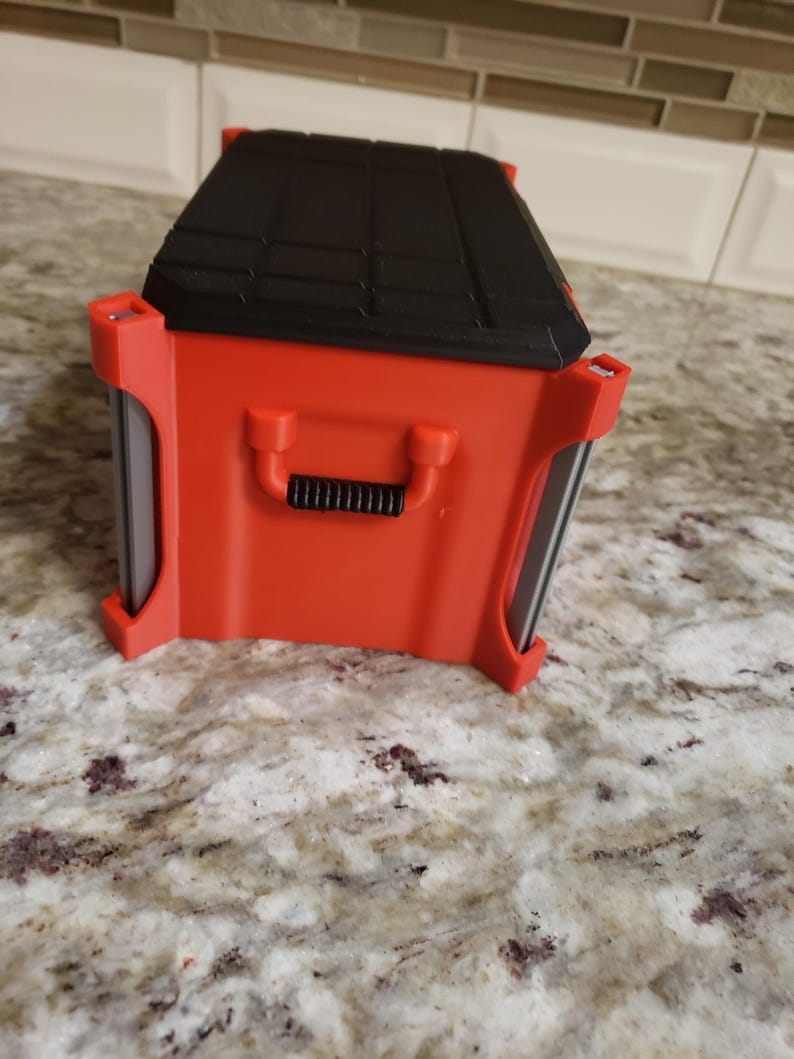 May include: A red and black toolbox with a handle. The toolbox has a black, textured lid and red sides. The handle is black and ribbed. The toolbox is on a speckled countertop.