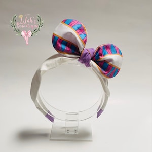 May include: White headband with a purple and pink patterned bow. The bow has white stripes and blue accents.