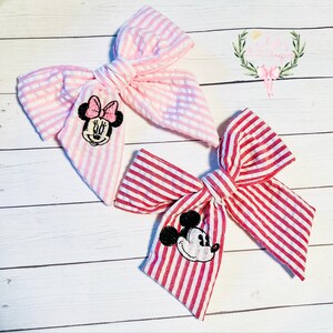 May include: Two fabric hair bows with red and white stripes and pink and white stripes. Each bow has an embroidered cartoon character, Mickey Mouse and Minnie Mouse.