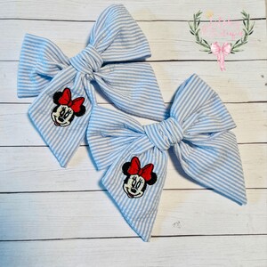 May include: Two blue and white striped fabric hair bows with a Minnie Mouse embroidery on each bow.
