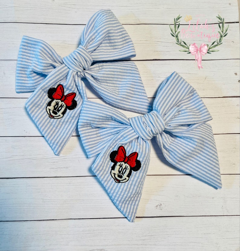 May include: Two blue and white striped fabric hair bows with a Minnie Mouse embroidery on each bow.