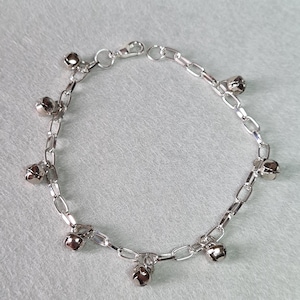 May include: A silver chain bracelet with multiple small silver bells attached. The bracelet is made of a delicate chain and has a lobster clasp closure.
